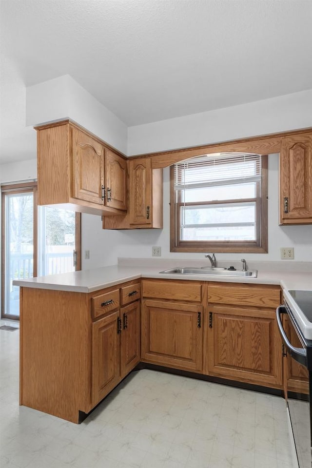 kitchen with a sink, range with electric stovetop, a peninsula, light countertops, and light floors