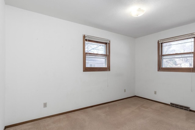 spare room with visible vents, light colored carpet, and baseboards