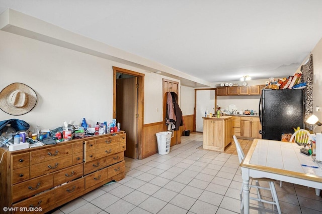 kitchen with wooden walls, a wainscoted wall, tile countertops, light tile patterned floors, and freestanding refrigerator