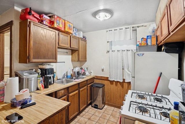 kitchen with brown cabinets, a sink, white appliances, light countertops, and light tile patterned floors