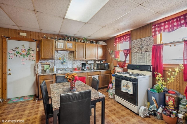 kitchen featuring light floors, wood walls, range with gas cooktop, and brown cabinets