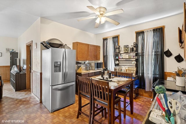 kitchen featuring a wainscoted wall, brown cabinetry, stainless steel refrigerator with ice dispenser, and ceiling fan