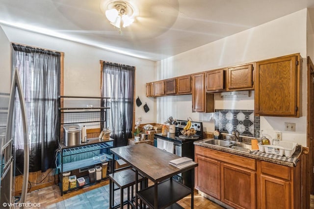 kitchen featuring dark countertops, stainless steel range with electric stovetop, brown cabinetry, and a sink