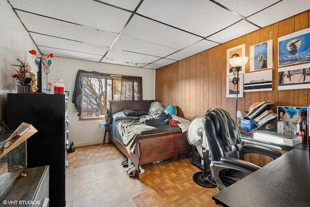 bedroom with tile patterned floors, a drop ceiling, wood walls, and freestanding refrigerator