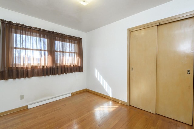 unfurnished bedroom featuring a closet, hardwood / wood-style flooring, baseboards, and a baseboard radiator