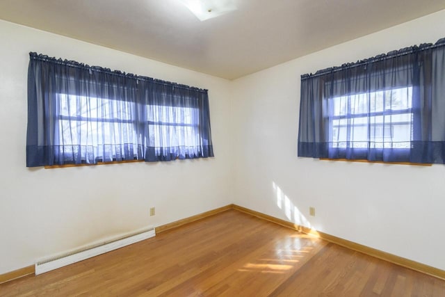 empty room featuring wood finished floors, baseboards, and a baseboard radiator