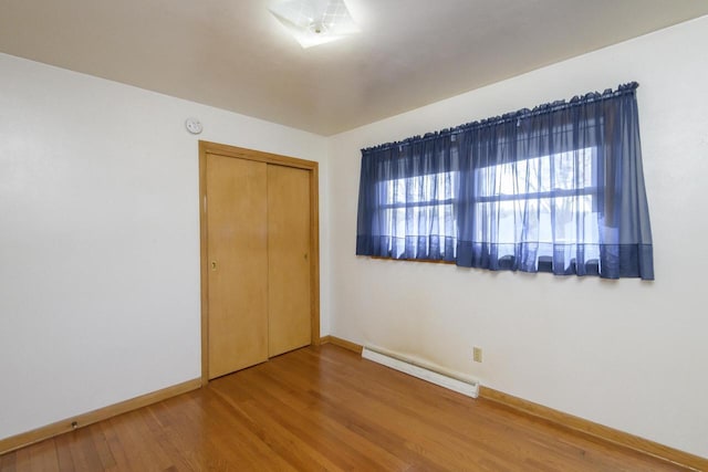 unfurnished bedroom featuring a baseboard radiator, baseboards, a closet, and wood finished floors