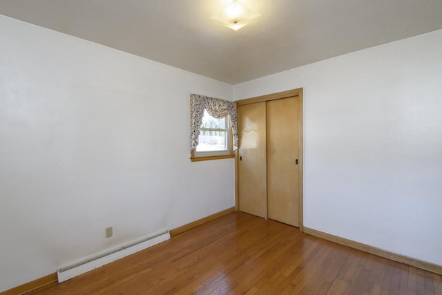 unfurnished bedroom featuring a baseboard radiator, wood-type flooring, baseboards, and a closet