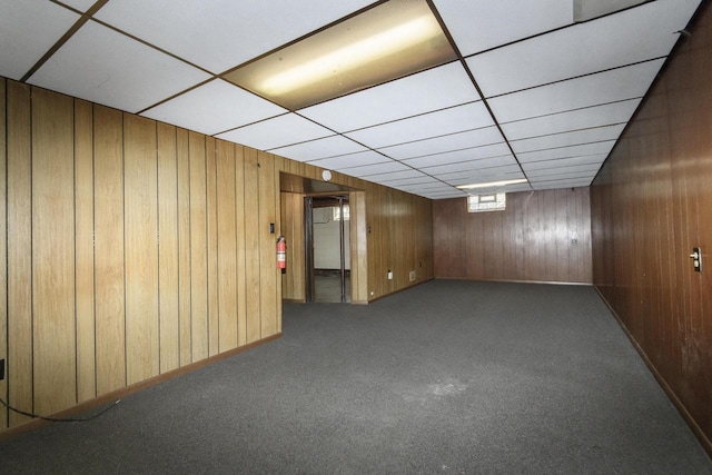 basement with a drop ceiling, wooden walls, and carpet flooring