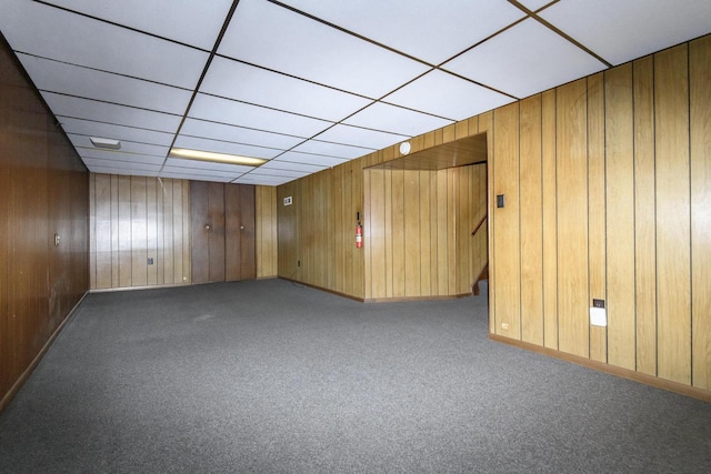 unfurnished room with carpet flooring, stairway, and wooden walls