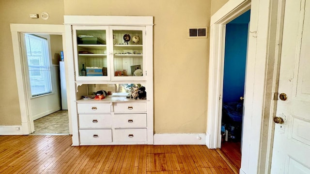 hall featuring hardwood / wood-style flooring, baseboards, and visible vents