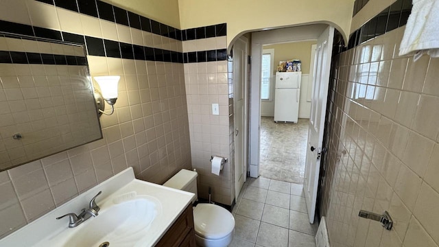 half bath featuring tile patterned flooring, toilet, tile walls, and vanity