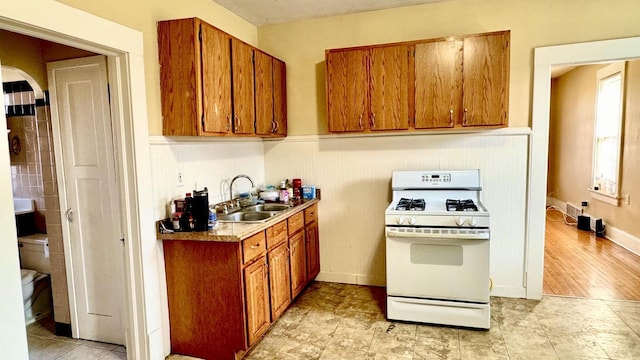 kitchen with arched walkways, a sink, brown cabinets, and white gas range oven