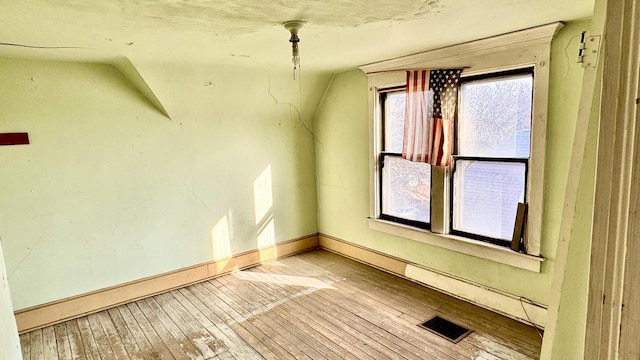 additional living space featuring hardwood / wood-style flooring, baseboards, visible vents, and vaulted ceiling