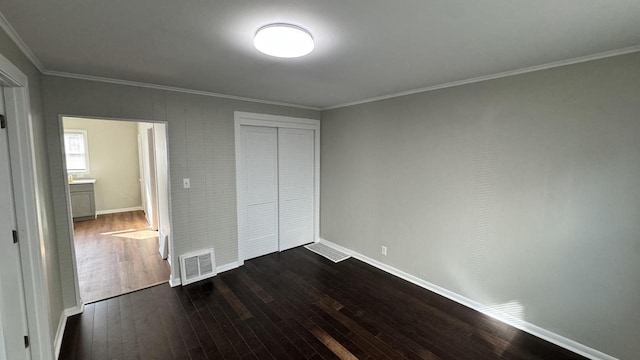 unfurnished bedroom with visible vents, baseboards, dark wood-type flooring, a closet, and crown molding