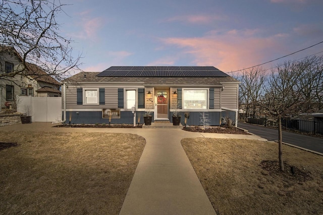 bungalow-style house with solar panels, fence, and a shingled roof