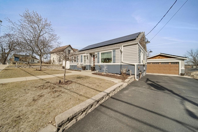 view of front facade featuring roof mounted solar panels, an outbuilding, roof with shingles, and a detached garage