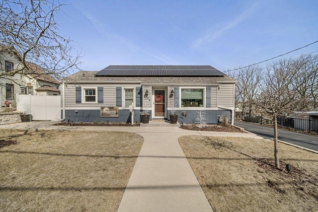 bungalow-style home featuring fence, roof mounted solar panels, and roof with shingles