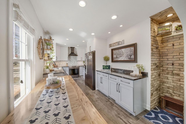 kitchen with stainless steel appliances, tasteful backsplash, light wood-style flooring, and wall chimney range hood