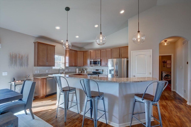 kitchen featuring visible vents, washer / dryer, wood finished floors, arched walkways, and stainless steel appliances