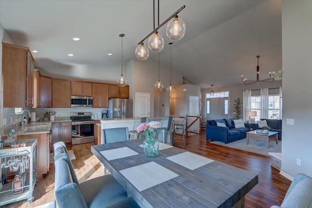 dining room with baseboards, recessed lighting, wood finished floors, a notable chandelier, and high vaulted ceiling