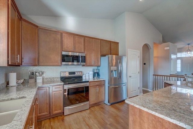 kitchen featuring arched walkways, light wood-style floors, appliances with stainless steel finishes, and brown cabinets