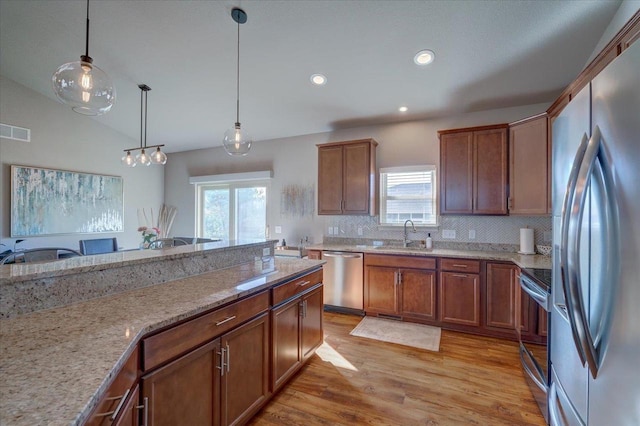 kitchen with visible vents, light stone counters, stainless steel appliances, light wood finished floors, and hanging light fixtures