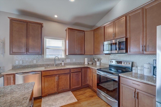 kitchen with backsplash, light wood-type flooring, lofted ceiling, stainless steel appliances, and a sink