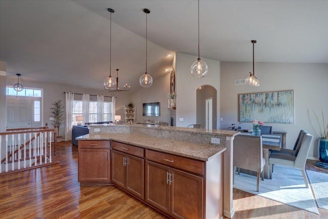 kitchen featuring brown cabinetry, light stone countertops, light wood finished floors, arched walkways, and open floor plan