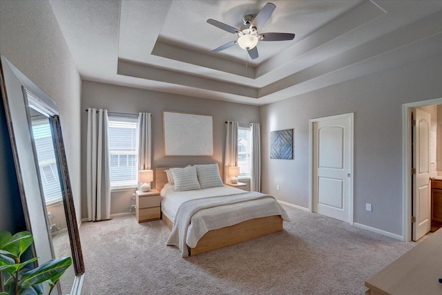 carpeted bedroom featuring ensuite bath, a raised ceiling, baseboards, and a ceiling fan