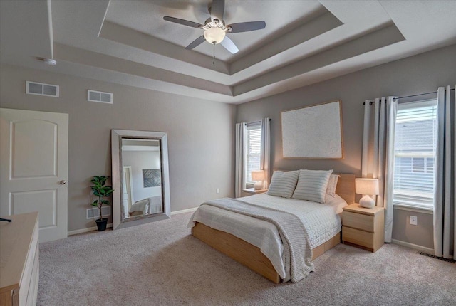 bedroom with a tray ceiling, light colored carpet, and visible vents