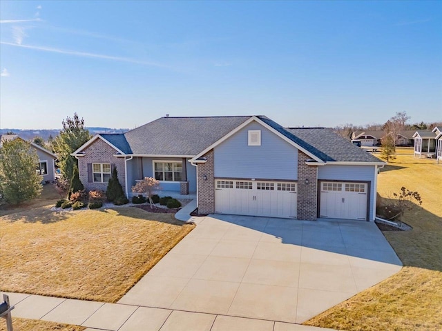 view of front facade with a front yard, driveway, an attached garage, a shingled roof, and brick siding