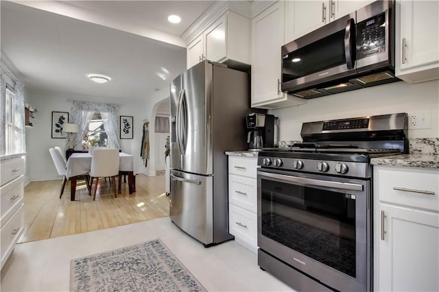 kitchen featuring light stone counters, white cabinets, appliances with stainless steel finishes, and arched walkways