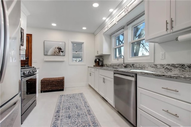 kitchen featuring light stone counters, freestanding refrigerator, white cabinets, stainless steel dishwasher, and gas range