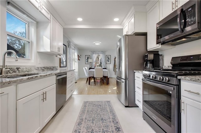 kitchen with a sink, light stone counters, appliances with stainless steel finishes, and white cabinets