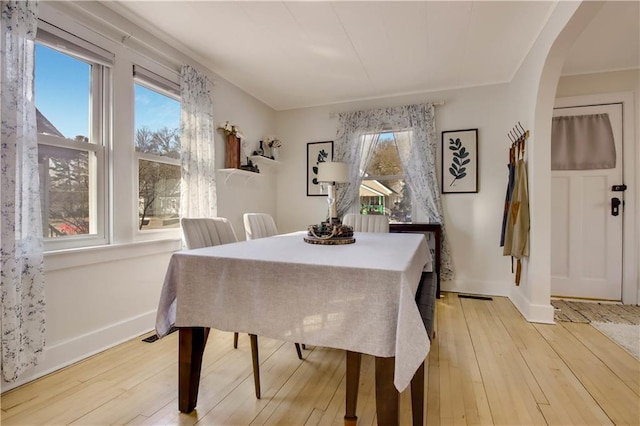 dining room featuring baseboards, arched walkways, and light wood finished floors