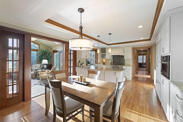 dining area featuring recessed lighting, light wood-style flooring, crown molding, and a raised ceiling