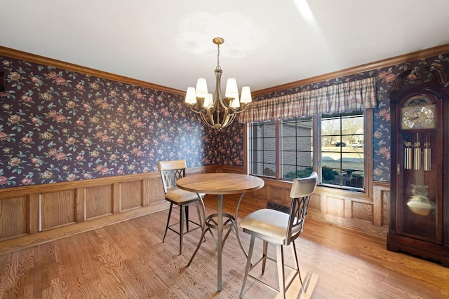 dining room with wood finished floors, a wainscoted wall, wallpapered walls, crown molding, and a chandelier