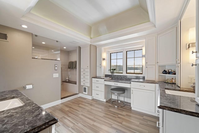 full bathroom featuring wood finished floors, baseboards, tiled shower, a tray ceiling, and crown molding