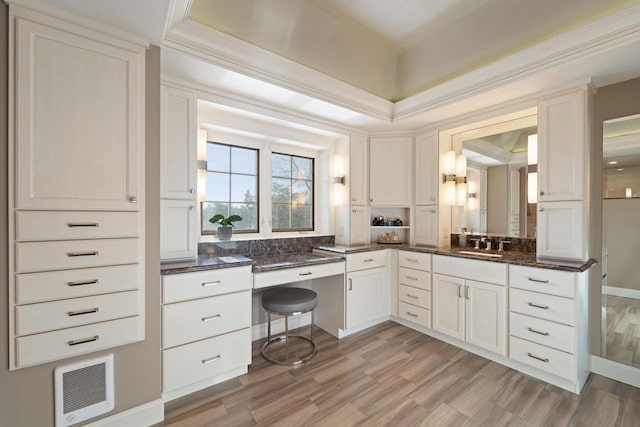 kitchen with dark stone counters, light wood-type flooring, white cabinets, built in study area, and a sink