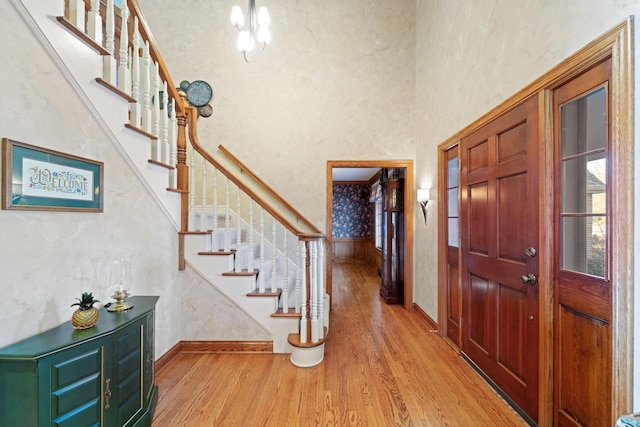 foyer featuring stairs, wood finished floors, wallpapered walls, and a chandelier