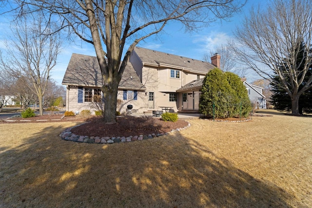 back of house featuring a yard, a patio area, a chimney, and a shingled roof