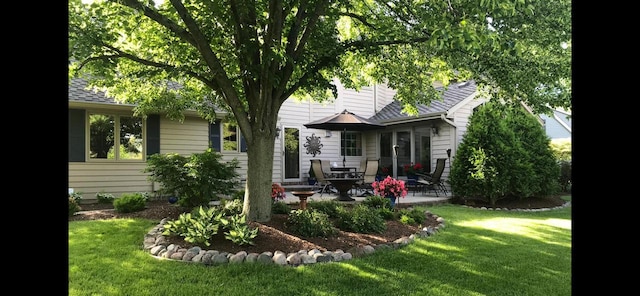 rear view of property with a lawn, a shingled roof, and a patio area