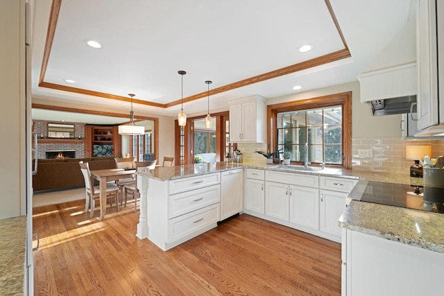 kitchen featuring a raised ceiling, a peninsula, light wood-style flooring, and white cabinets