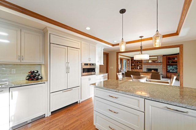 kitchen featuring light wood finished floors, paneled built in fridge, ornamental molding, stainless steel oven, and a raised ceiling