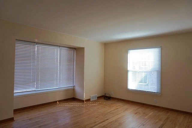 empty room with wood finished floors, visible vents, and baseboards