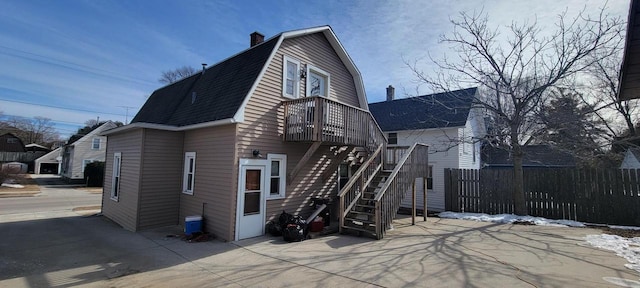 back of house featuring a shingled roof, fence, a gambrel roof, stairs, and a chimney