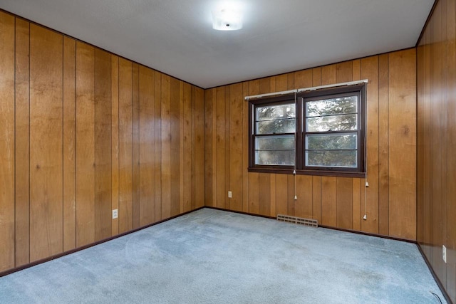 empty room with visible vents, carpet flooring, and wood walls