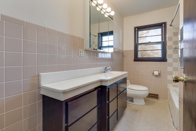 bathroom featuring visible vents, toilet, vanity, a bathing tub, and tile walls