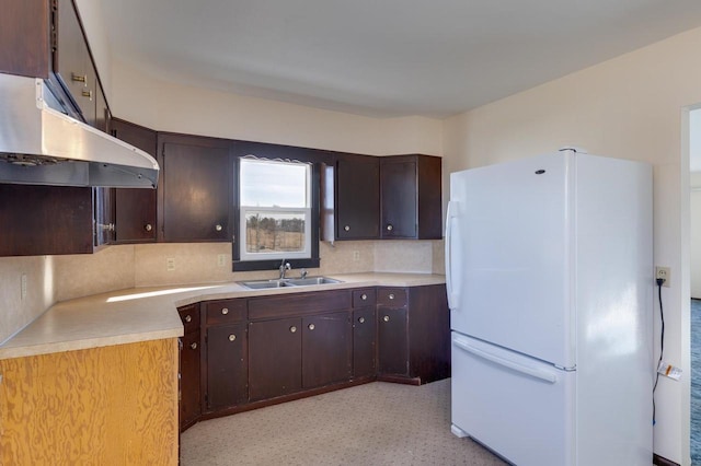 kitchen with a sink, tasteful backsplash, freestanding refrigerator, light countertops, and dark brown cabinets